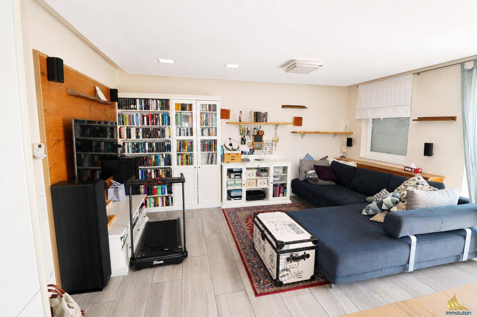 Geräumiges Wohnzimmer mit großem Sofa, Bücherregalen und einem Laufband für Fitness.