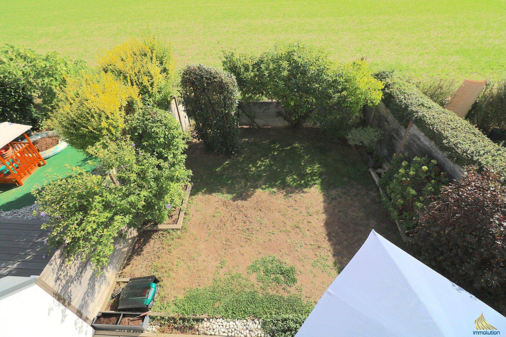 Gepflegter Gartenbereich mit Rasenfläche, Sträuchern und kleinem Spielplatz von oben.