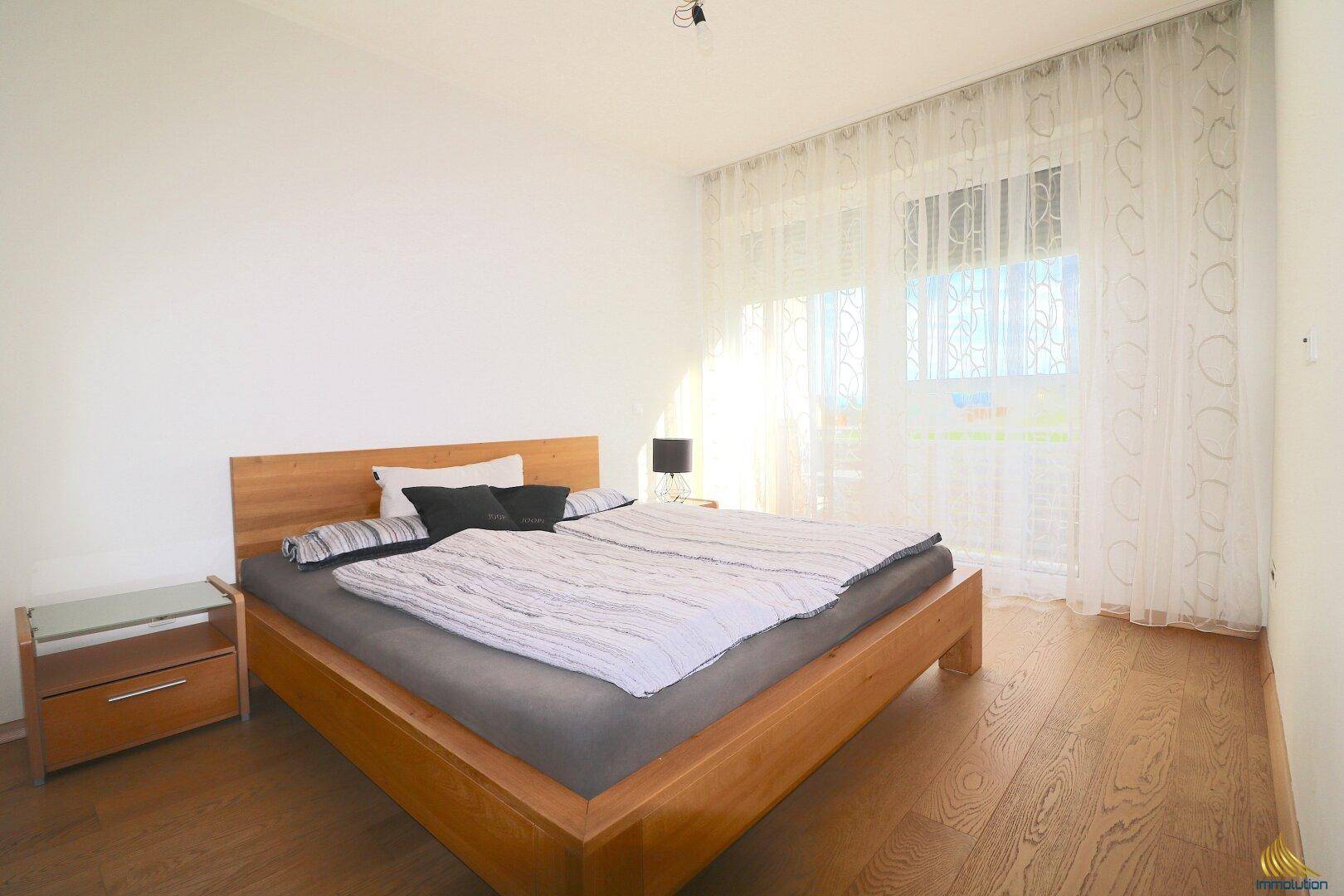Gemütliches Schlafzimmer mit Holzbett, Holzboden und großen Fenstern für eine helle Atmosphäre.