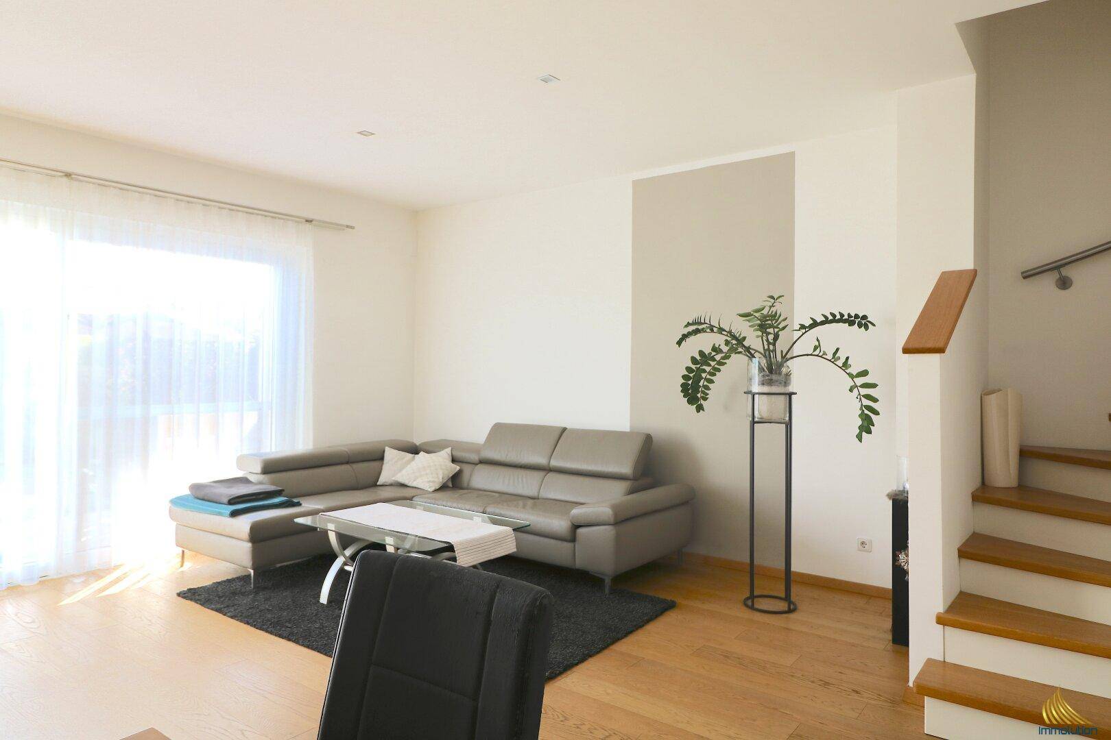 Helles Wohnzimmer mit beigem Ecksofa, Holzboden und großen Fenstern für viel Tageslicht.