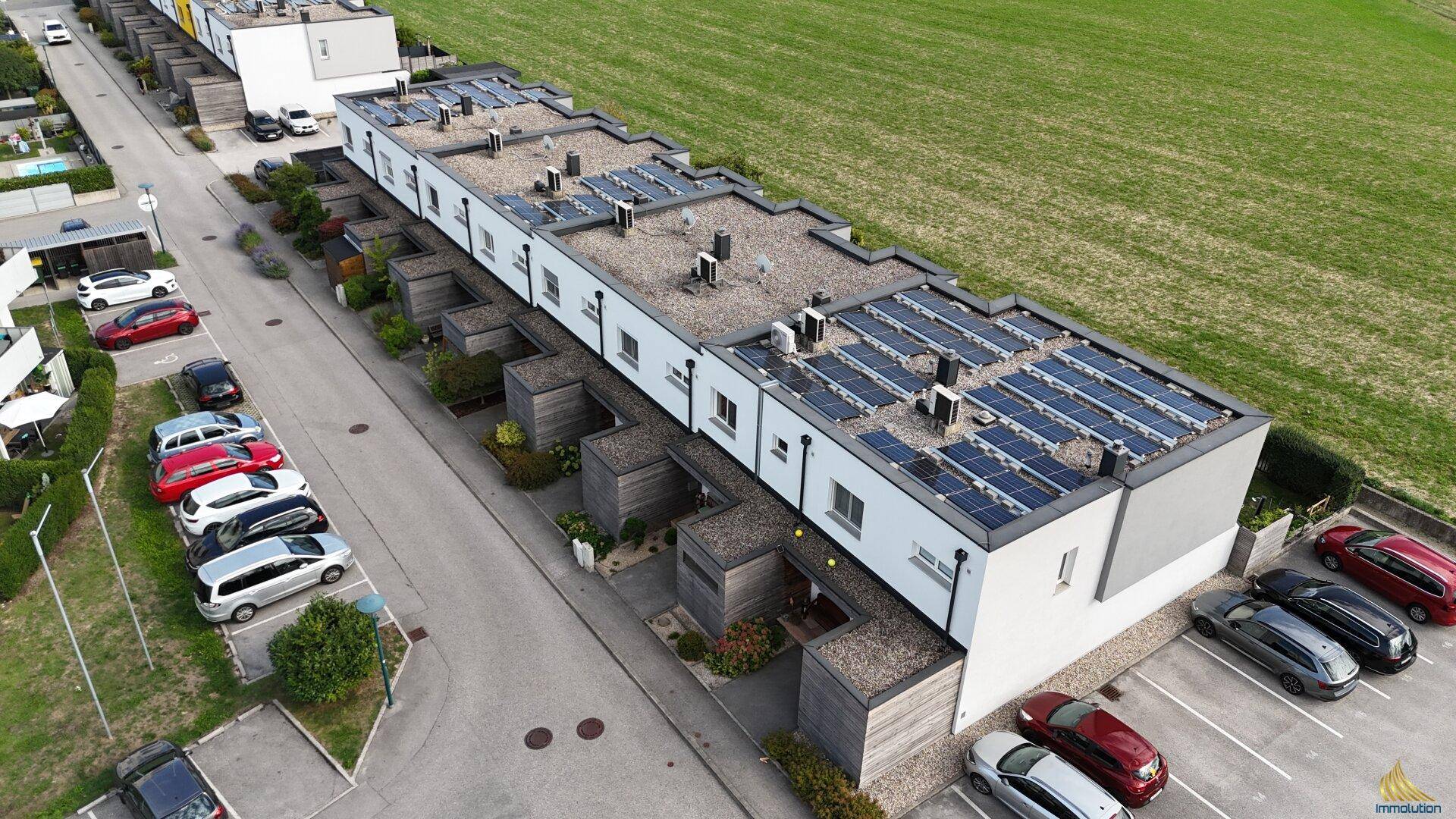Reihenhäuser mit modernen Flachdächern und installierten Solarmodulen aus der Vogelperspektive.