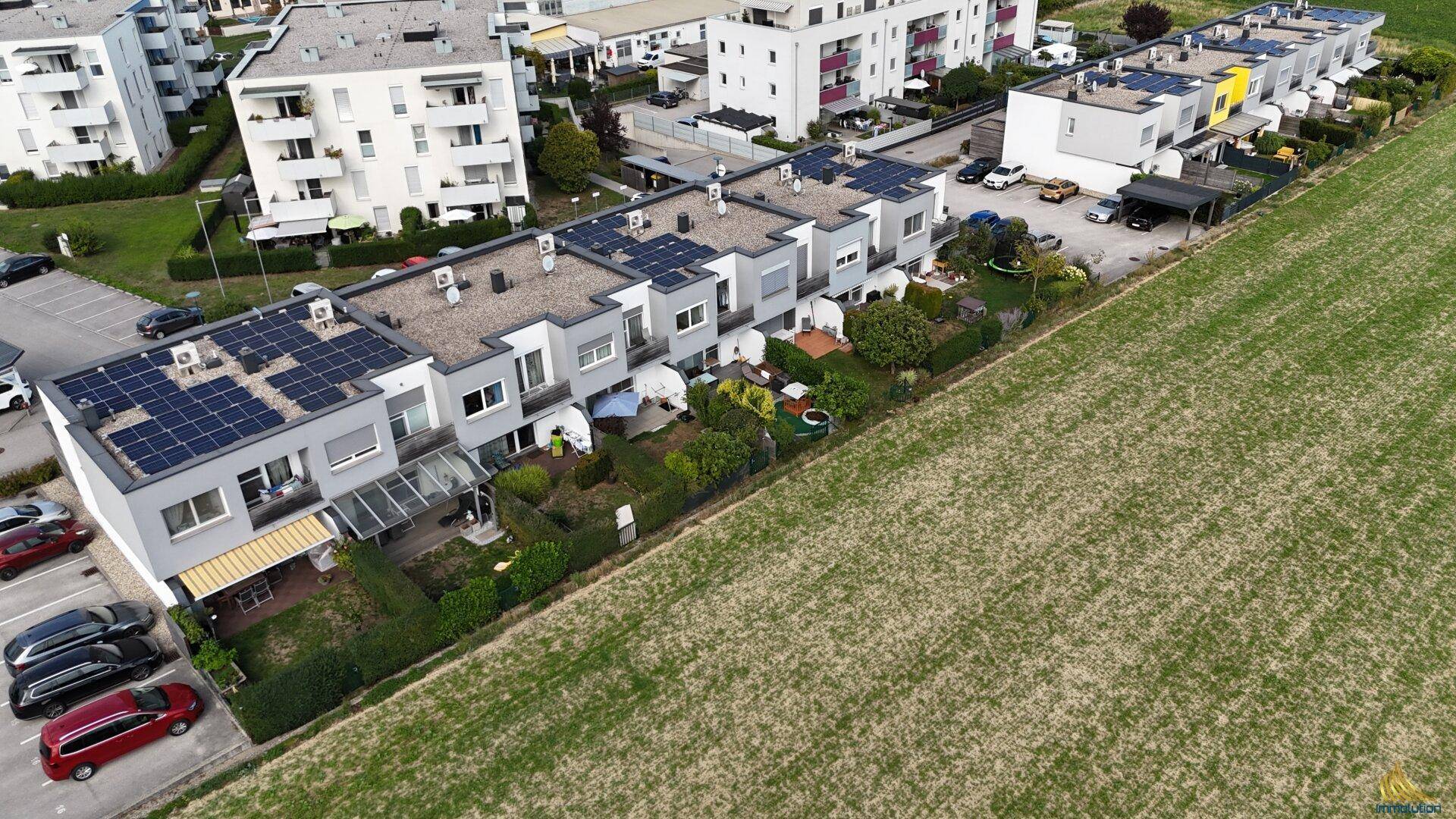 Luftaufnahme von modernen Reihenhäusern mit Photovoltaikanlagen auf den Dächern und Grünflächen.