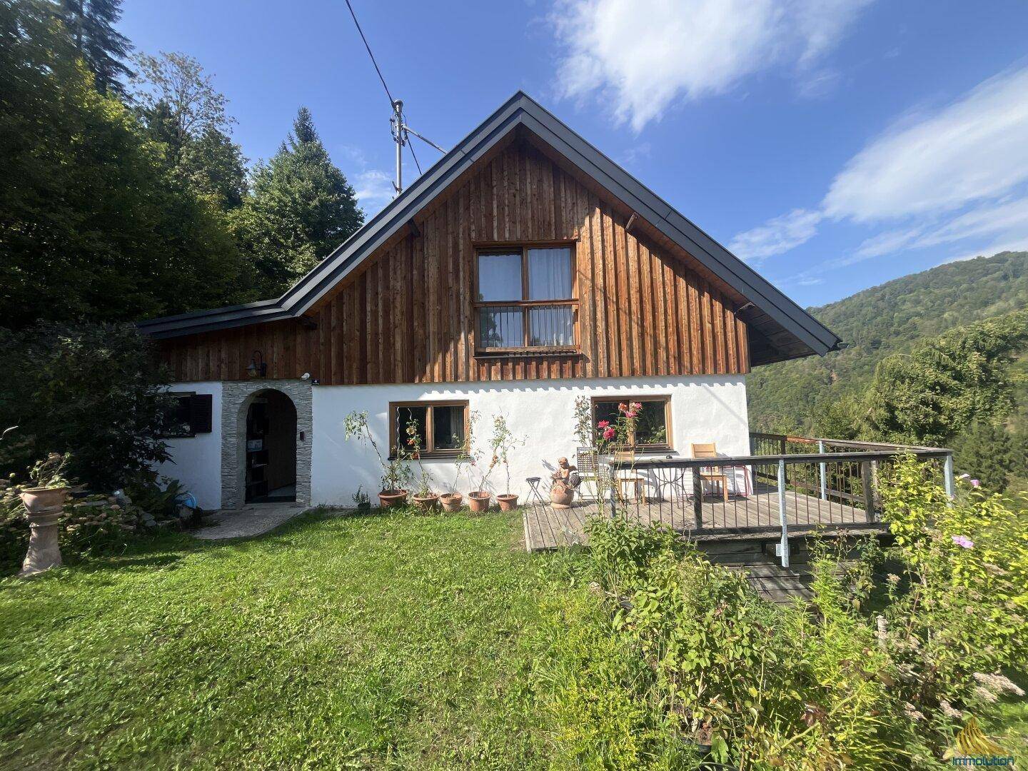 Idyllisches Landhaus mit Holzverkleidung und sonniger Terrasse, umgeben von üppiger Natur.