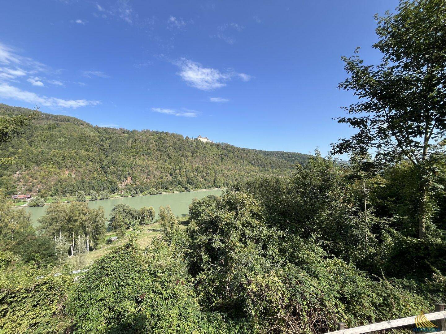 Weitläufiger Blick über einen Fluss und bewaldete Hügel unter strahlend blauem Himmel.