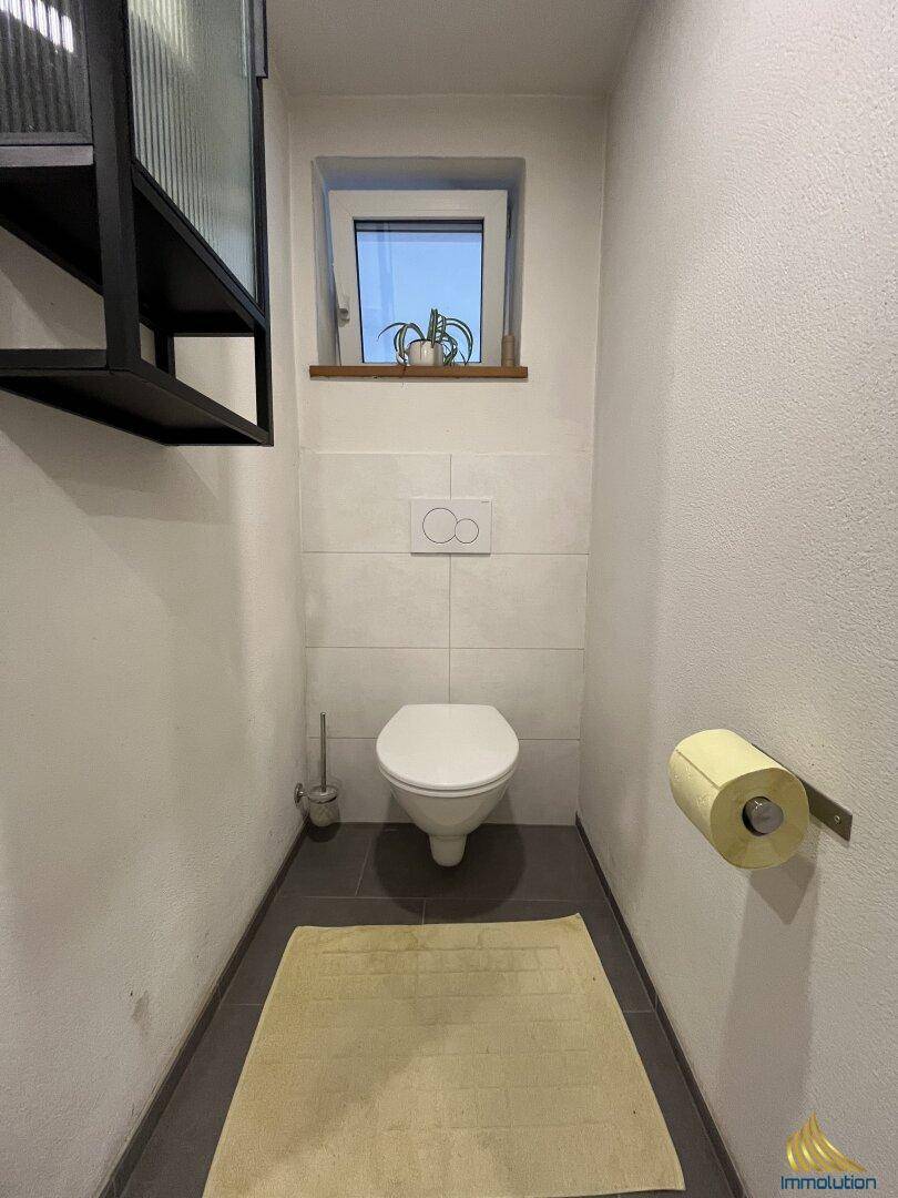 Kompaktes Gäste-WC mit wandhängender Toilette und kleinem Fenster für Belüftung.