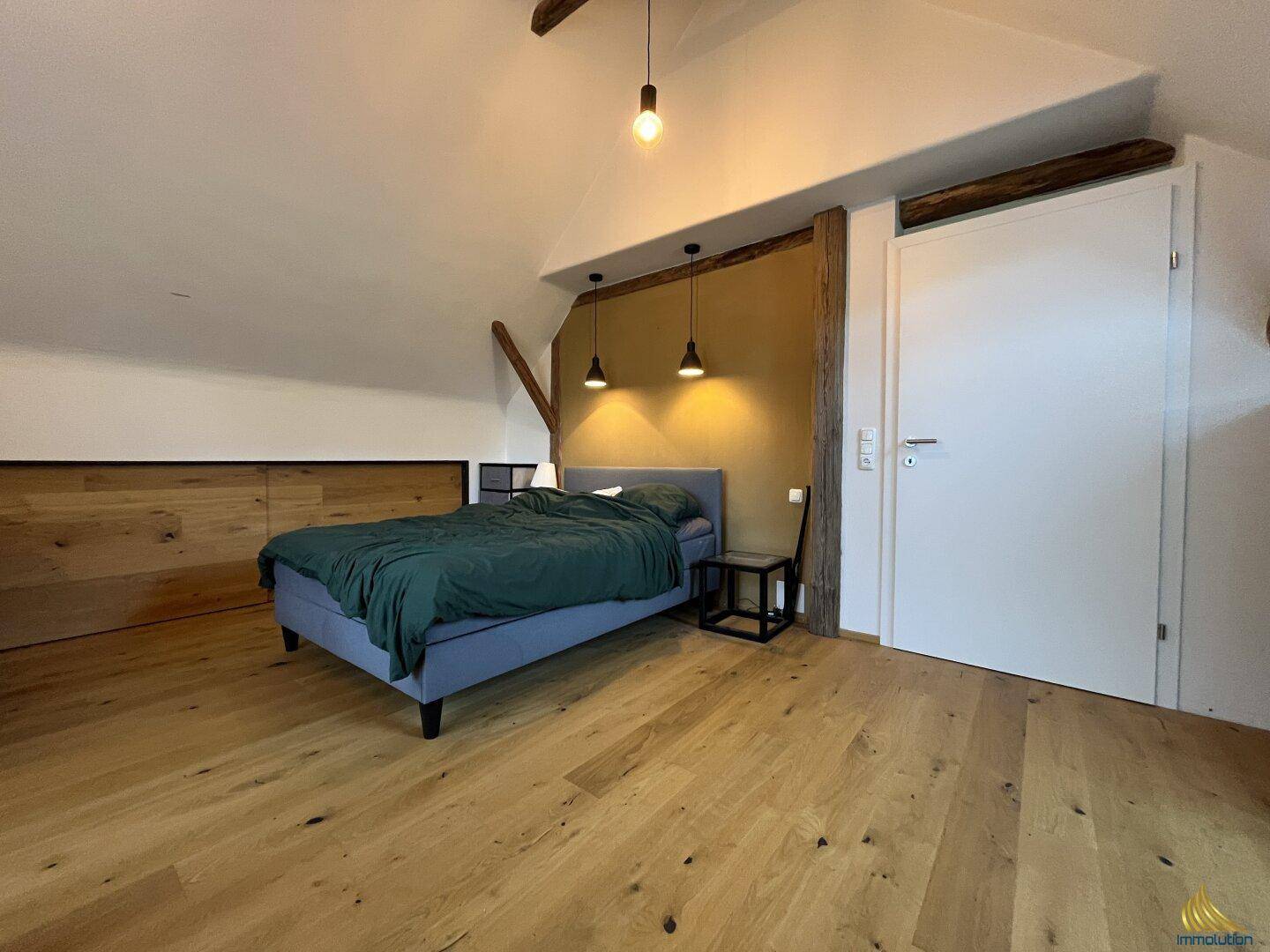 Helles Schlafzimmer mit Holzboden, sichtbaren Deckenbalken und Dachschräge für gemütliche Atmosphäre.