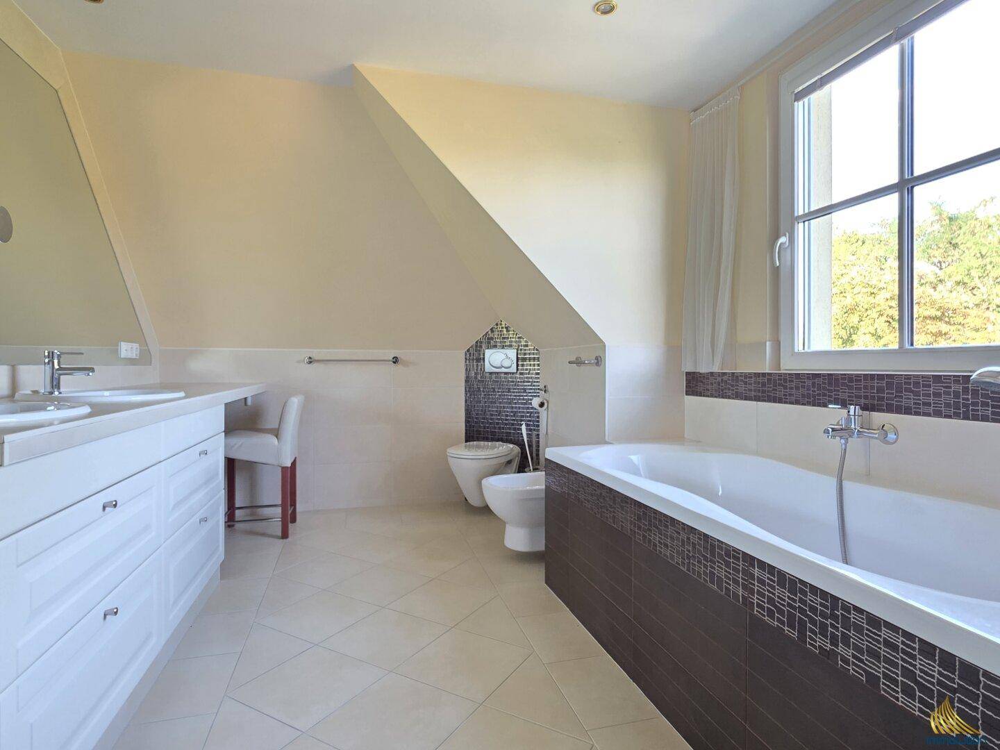 Helles Badezimmer im Dachgeschoss mit Badewanne, Doppelwaschbecken, WC, Bidet und großem Fenster.