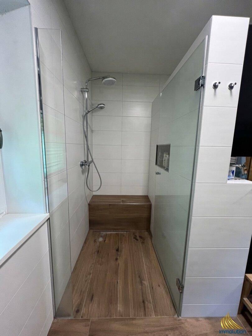 Geräumige begehbare Dusche mit Glasabtrennung und integrierter Holzbank für Komfort.