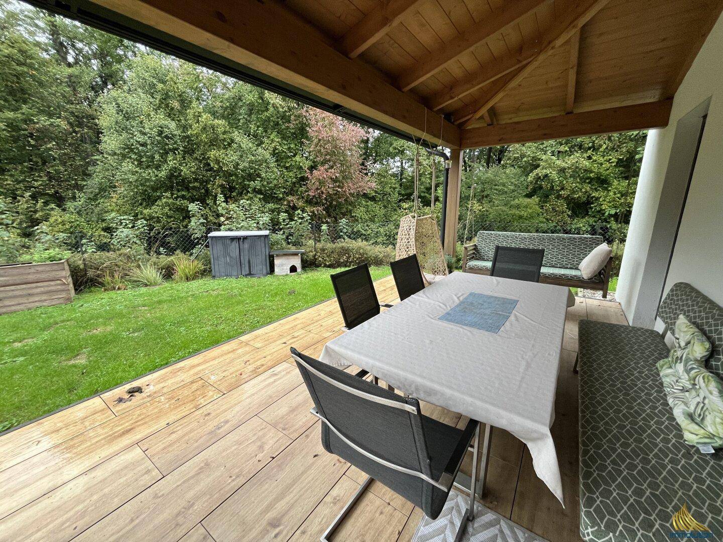 Überdachte Holzterrasse mit Esstisch und Gartenblick, ideal für Mahlzeiten im Freien.