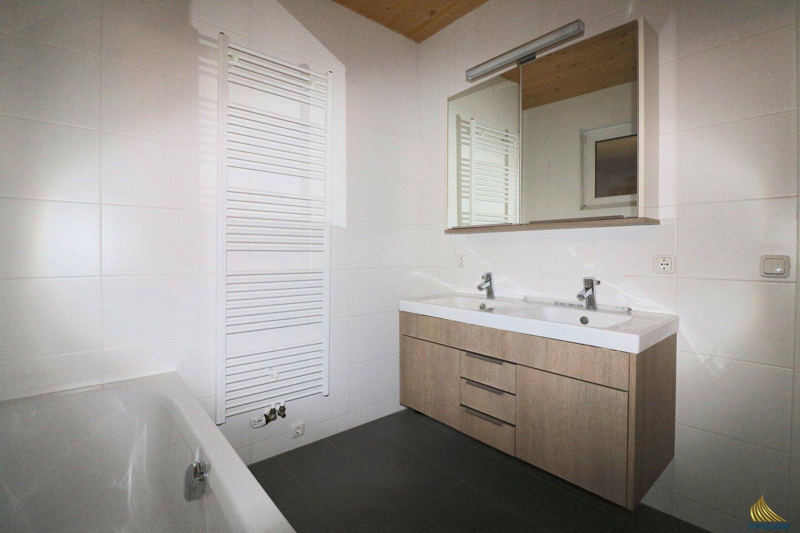 Modernes Badezimmer mit Doppelwaschbecken, Badewanne und beheiztem Handtuchhalter.