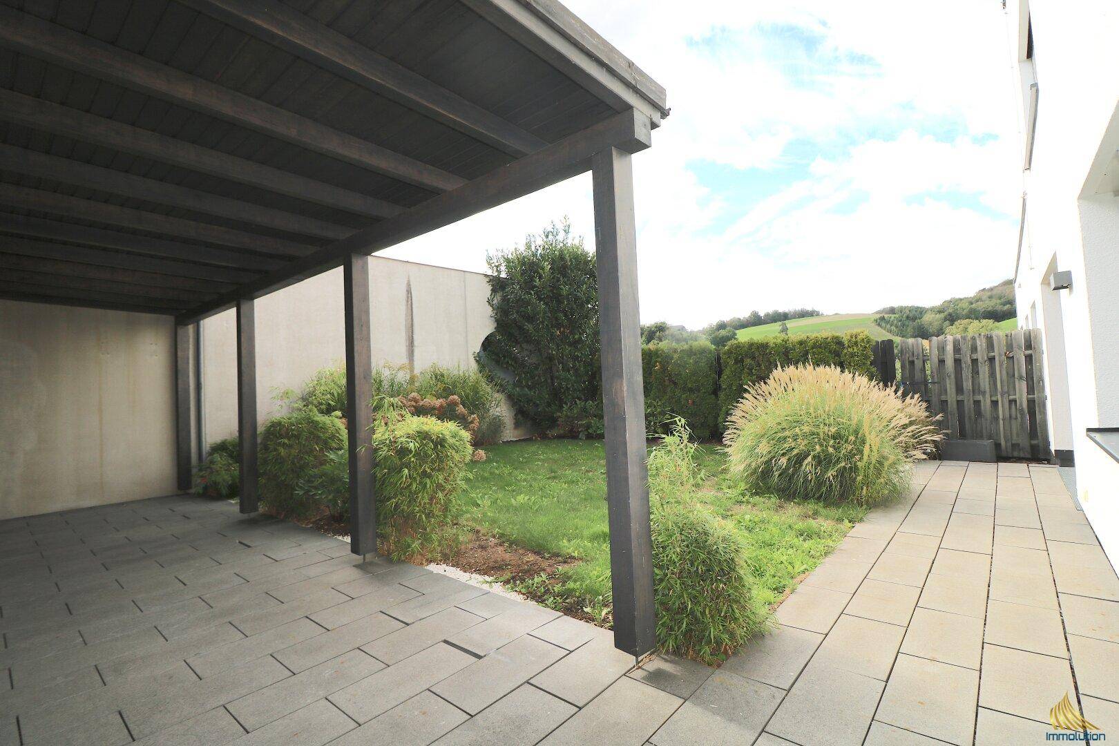 Überdachte Terrasse mit Garten und Blick auf die umliegende Landschaft, ideal für Entspannung im Freien.