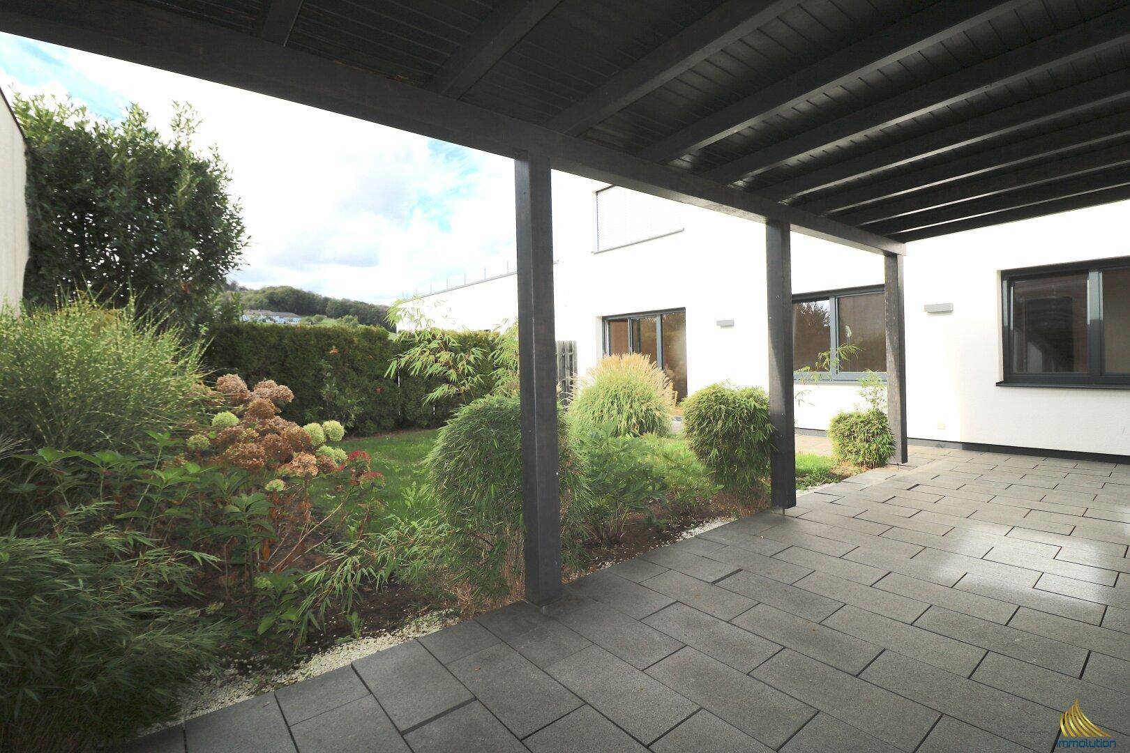 Überdachte Terrasse mit Blick auf den gepflegten Garten und die moderne Gebäudefassade.