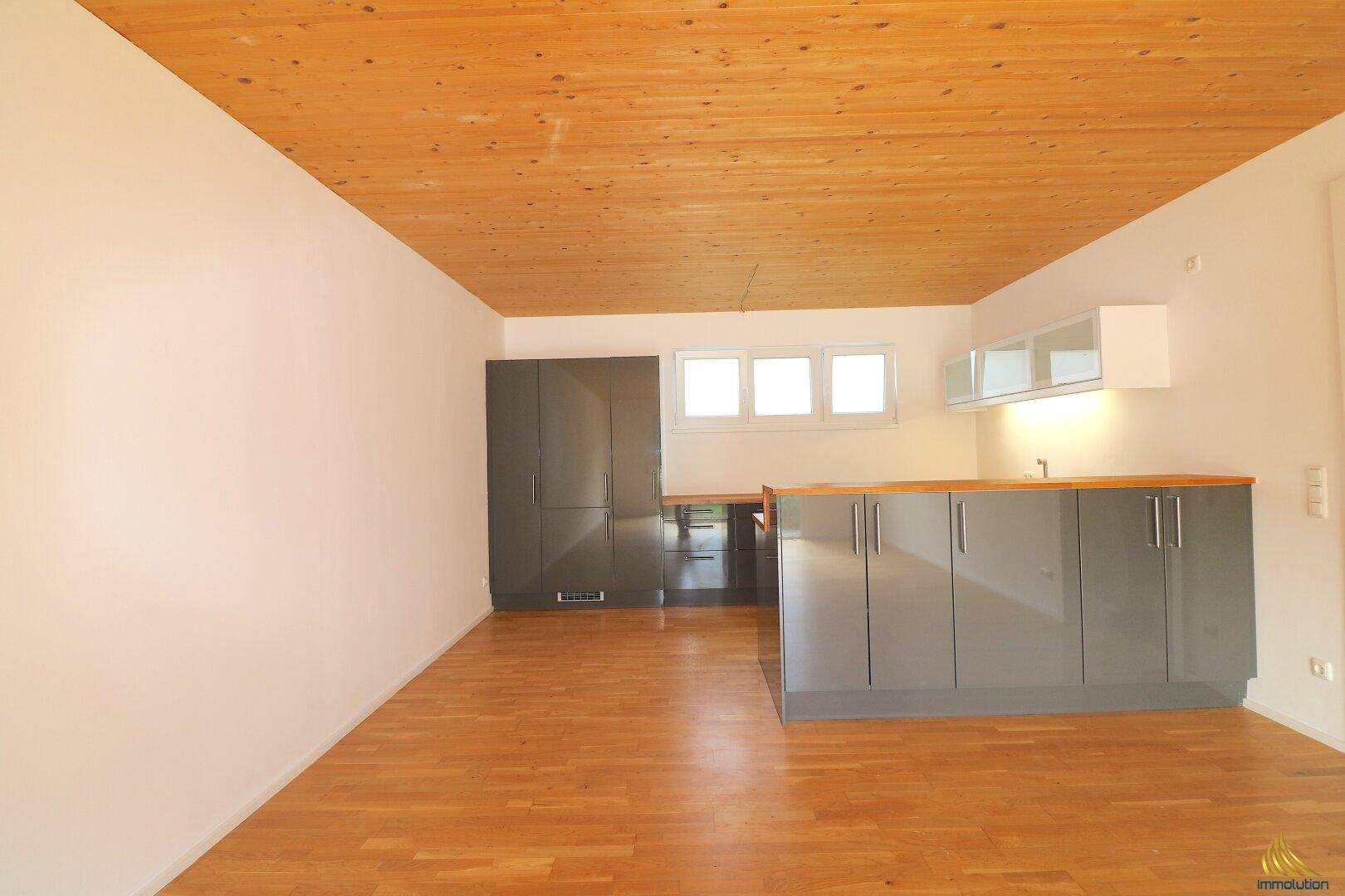Geräumige Küche mit Holzdecke und hellem Holzboden, ausgestattet mit modernen grauen Schränken.