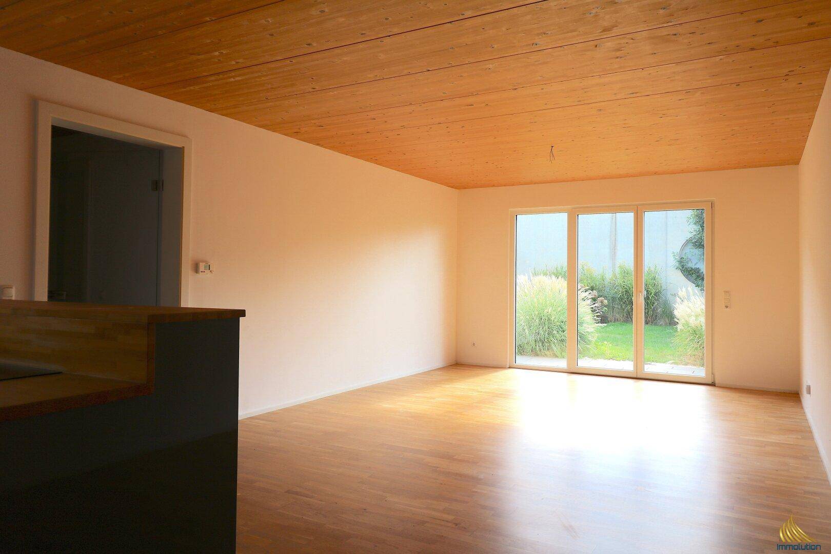 Helles Wohnzimmer mit Holzboden, Holzdecke und großen Glasschiebetüren zum Garten.