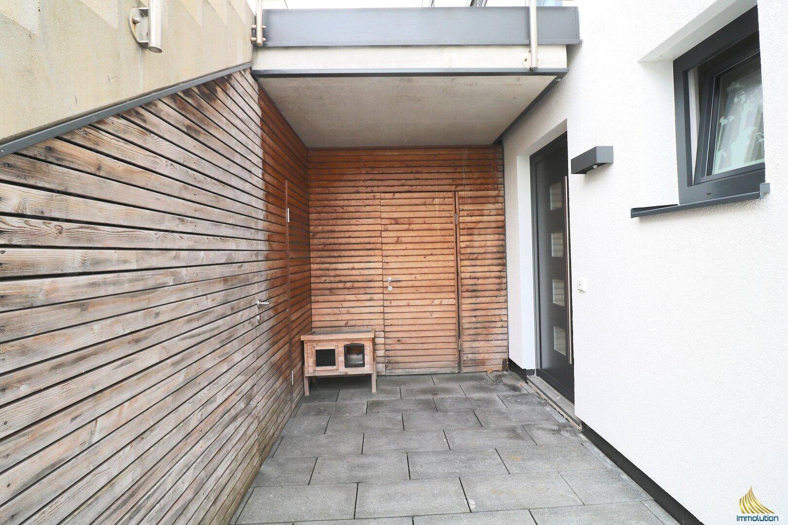 Überdachter Eingangsbereich mit Holzverkleidung und modernen Bodenfliesen.