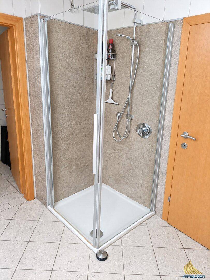 Badezimmer mit einer Eckduschkabine und hellen Fliesen, praktisch eingerichtet.