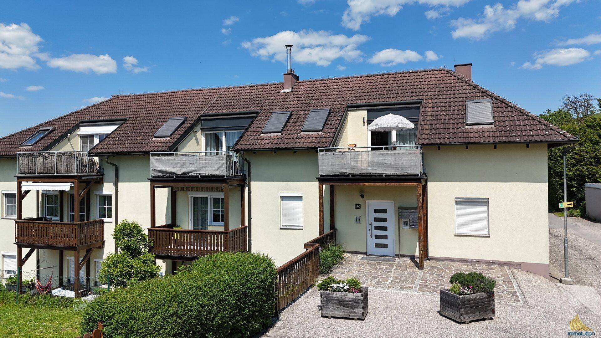 Mehrstöckiges Wohngebäude mit Balkonen, Satteldach und gepflegter Außenanlage.