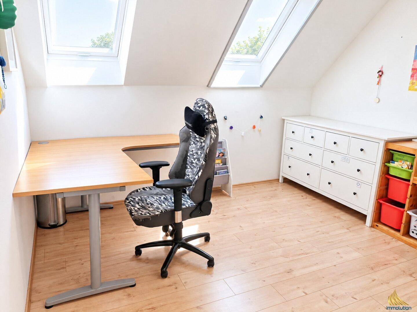 Helles Arbeitszimmer im Dachgeschoss mit Schreibtisch, Kommode und zwei Dachfenstern.