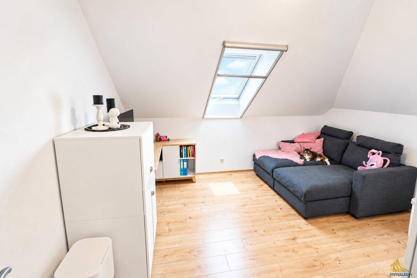 Gemütlicher Wohnbereich im Dachgeschoss mit Sofa, Schrank und Dachfenster.