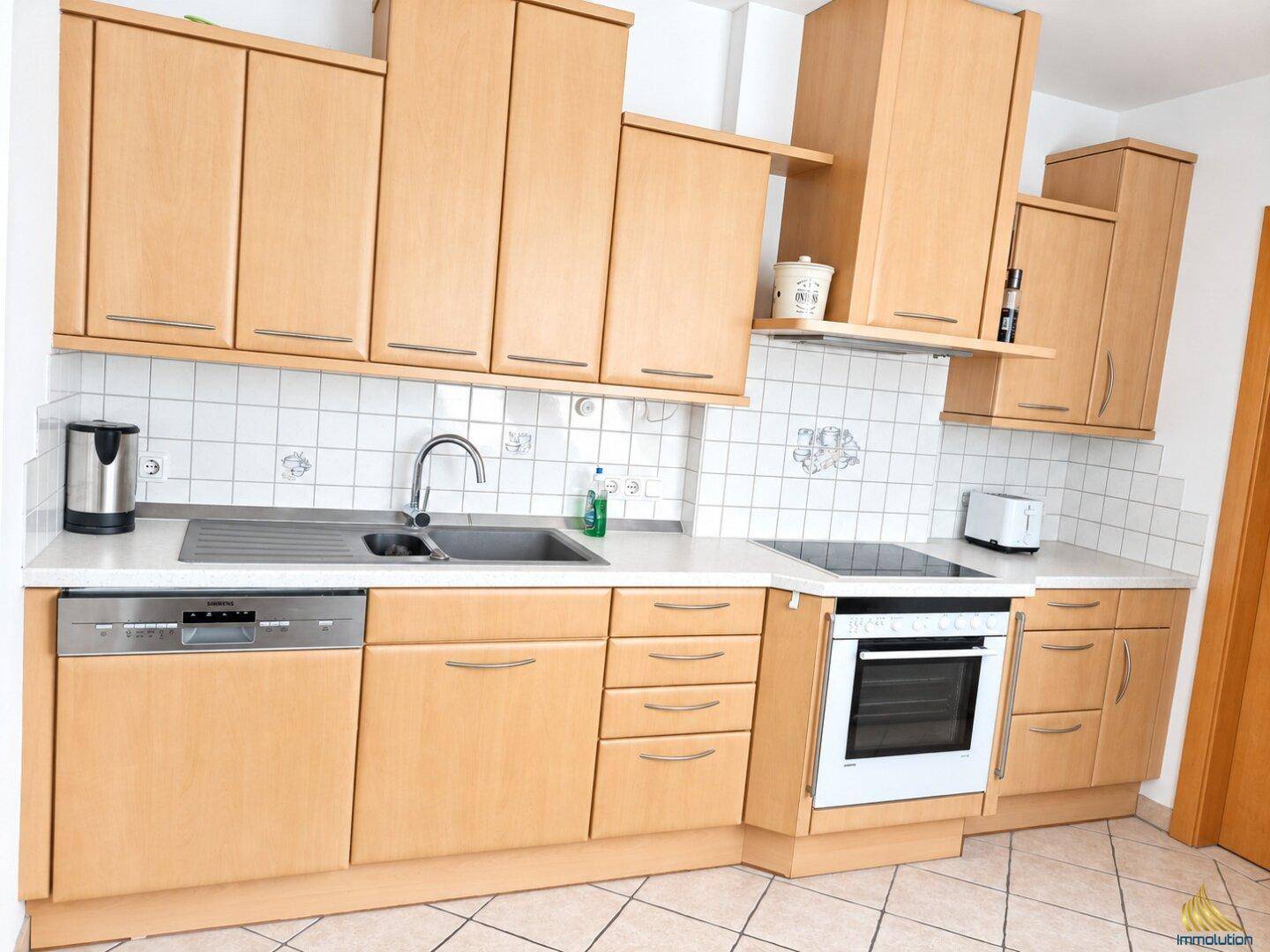 Helle Küche mit Holzschränken, weißen Arbeitsplatten und modernen Einbaugeräten.