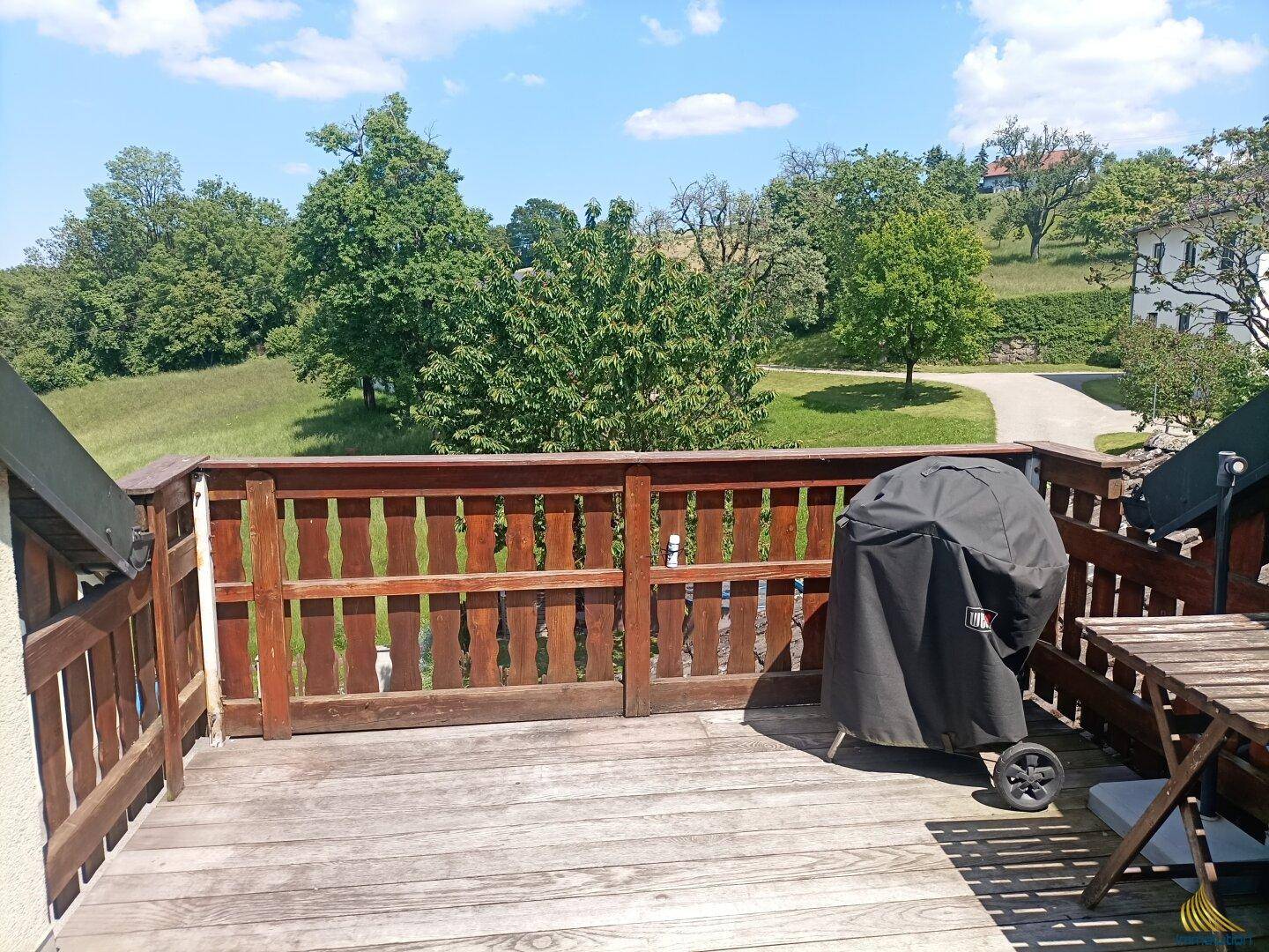 Holzterrasse mit Grill und weitem Blick ins Grüne und auf die umliegende Landschaft.