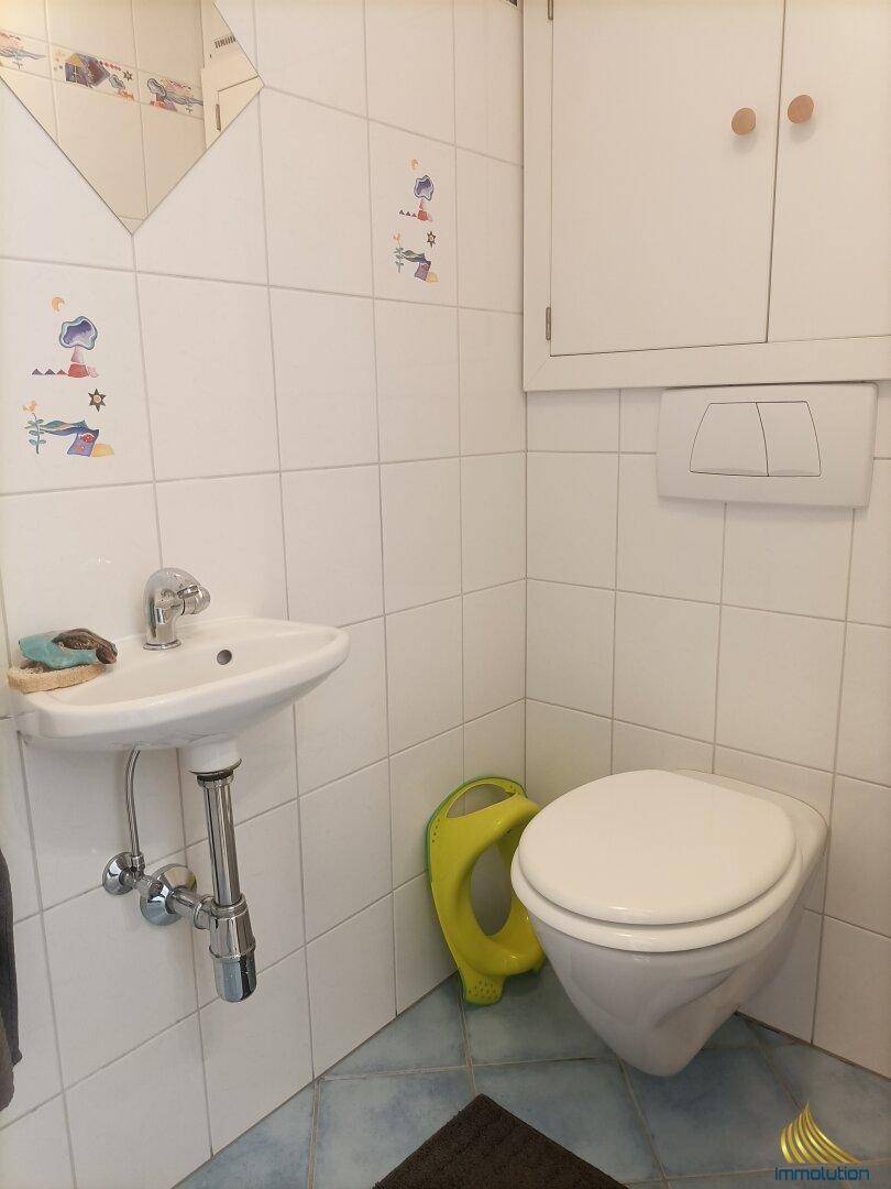 Kleines Gäste-WC mit wandhängender Toilette, kleinem Waschbecken und Fliesen.