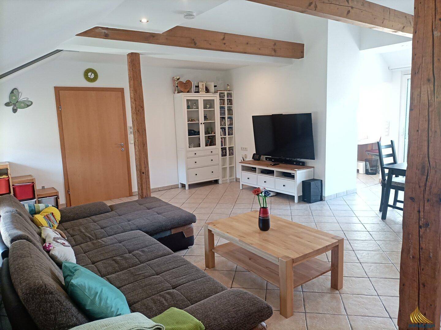 Gemütliches Wohnzimmer mit großem Sofa, Holzbalken und Fliesenboden.