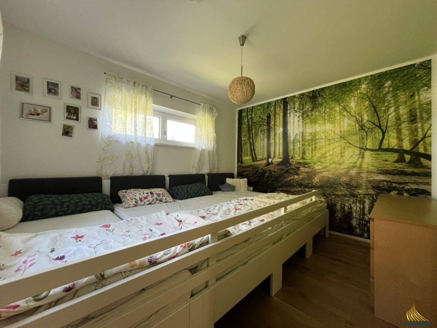 Schlafzimmer mit mehreren Betten und einer beeindruckenden Waldtapete, die eine natürliche Atmosphäre schafft.