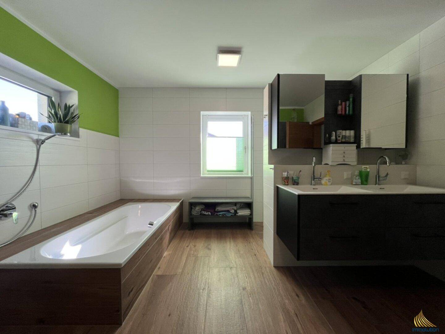 Modernes Badezimmer mit Badewanne, Doppelwaschbecken und grüner Akzentwand, hell und geräumig.