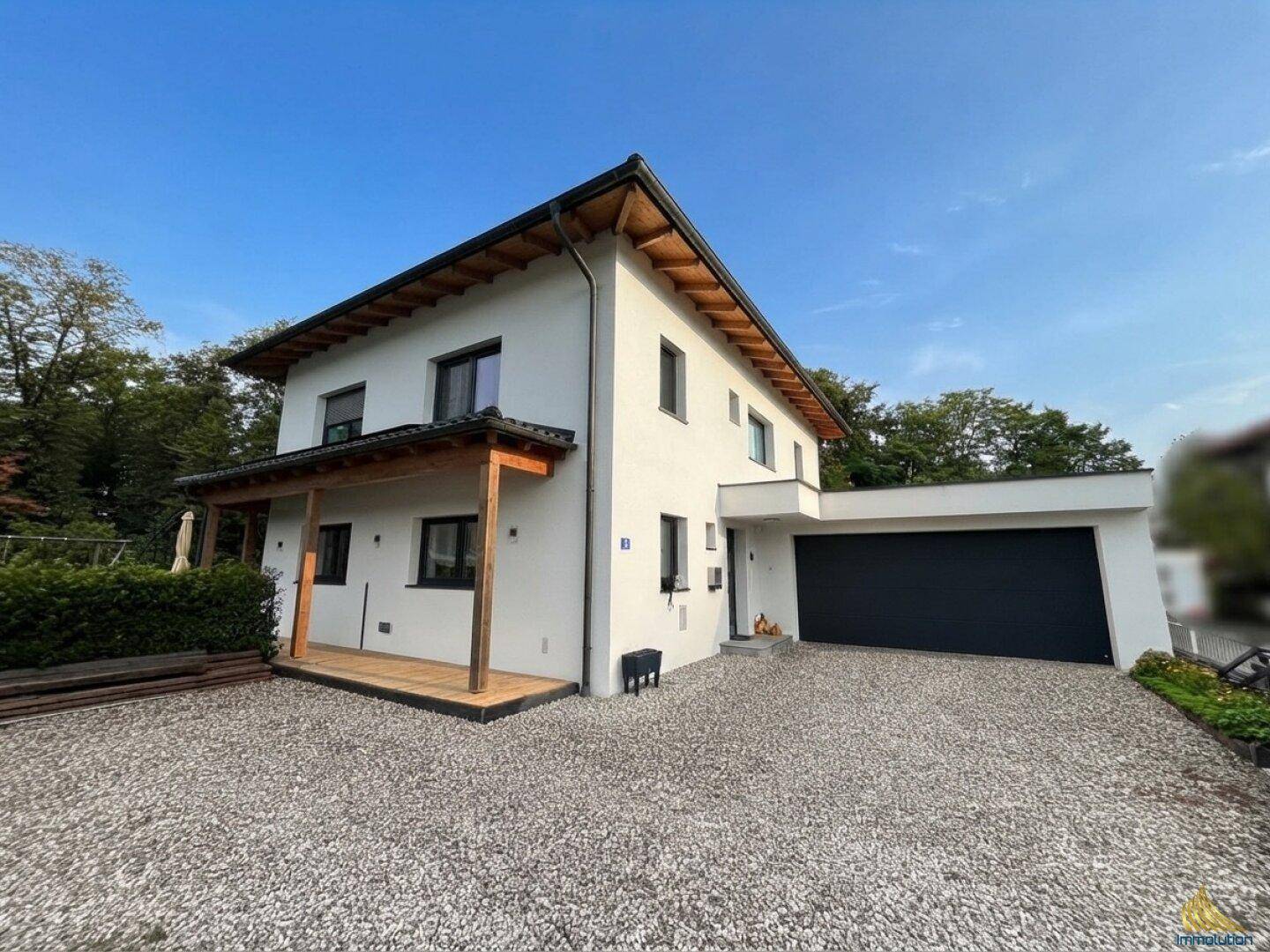 Seitenansicht des modernen Einfamilienhauses mit überdachter Holzveranda und integrierter Doppelgarage.