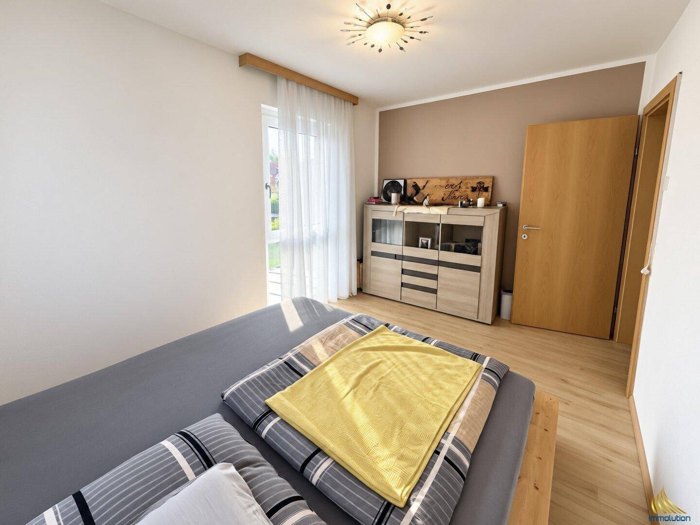 Gemütliches Schlafzimmer mit hellem Laminatboden, Fenster und Zugang zum Außenbereich.