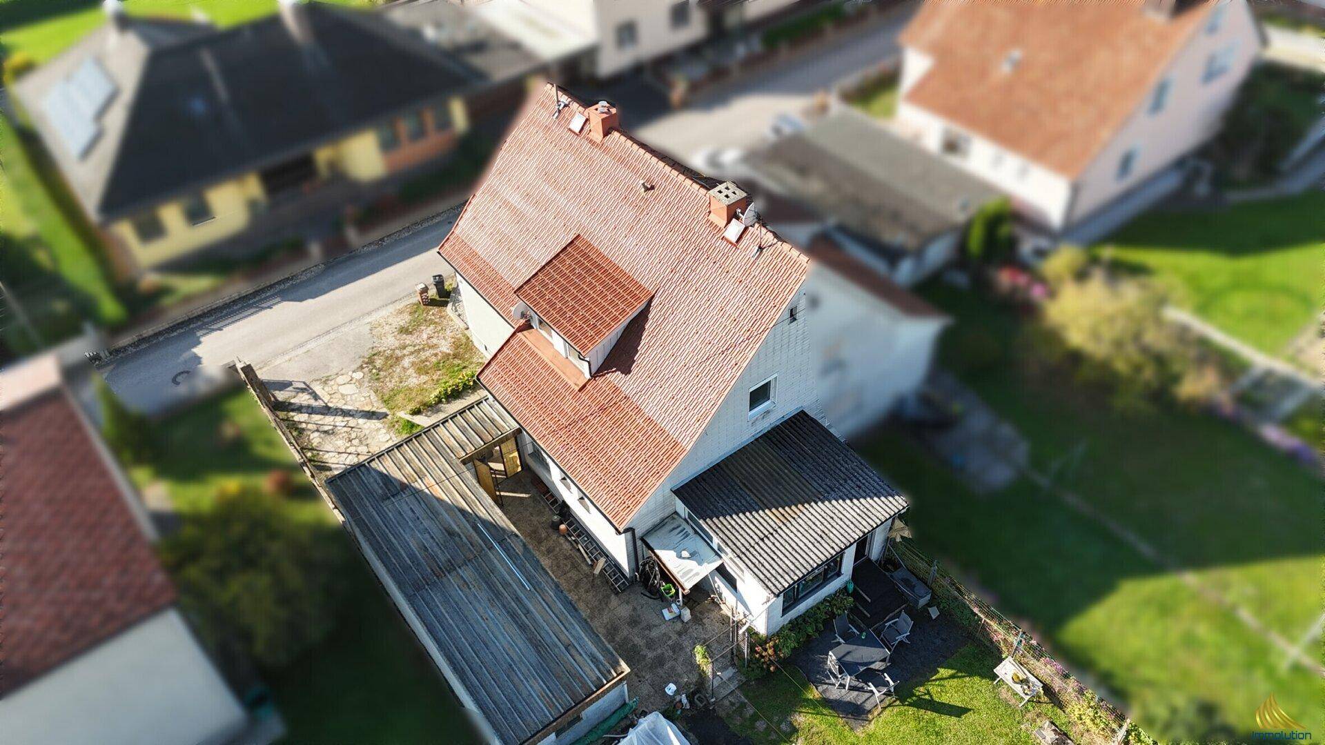 Dachansicht des Hauses mit überdachter Terrasse, Nebengebäuden und Blick ins Grüne.