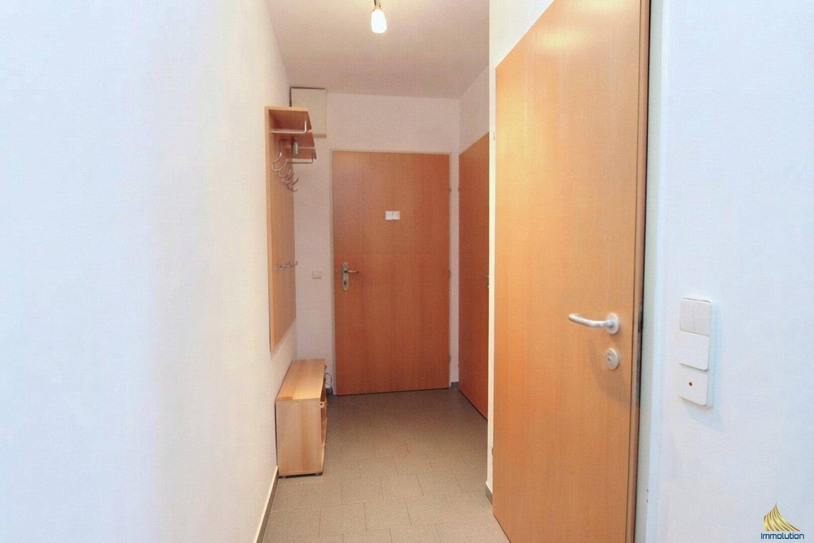 Eingangsbereich einer Wohnung mit Holztüren, Garderobe und einer kleinen Sitzbank.