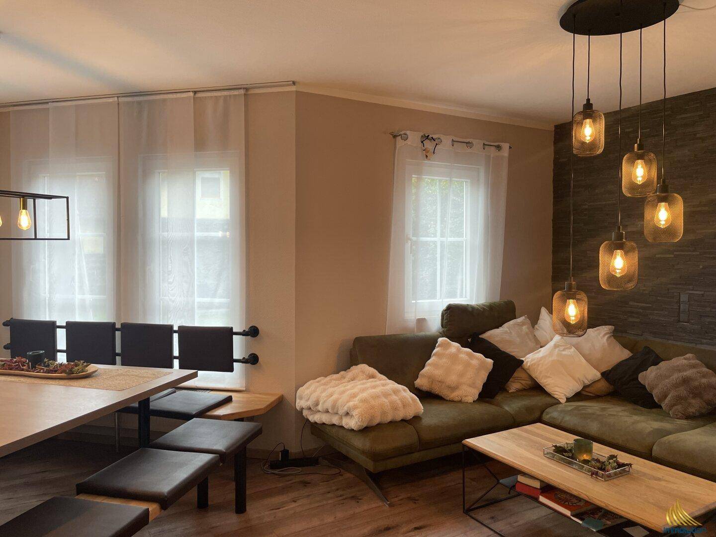 Heller Wohnbereich mit beigem Sofa, Holzboden und modernen Hängelampen.