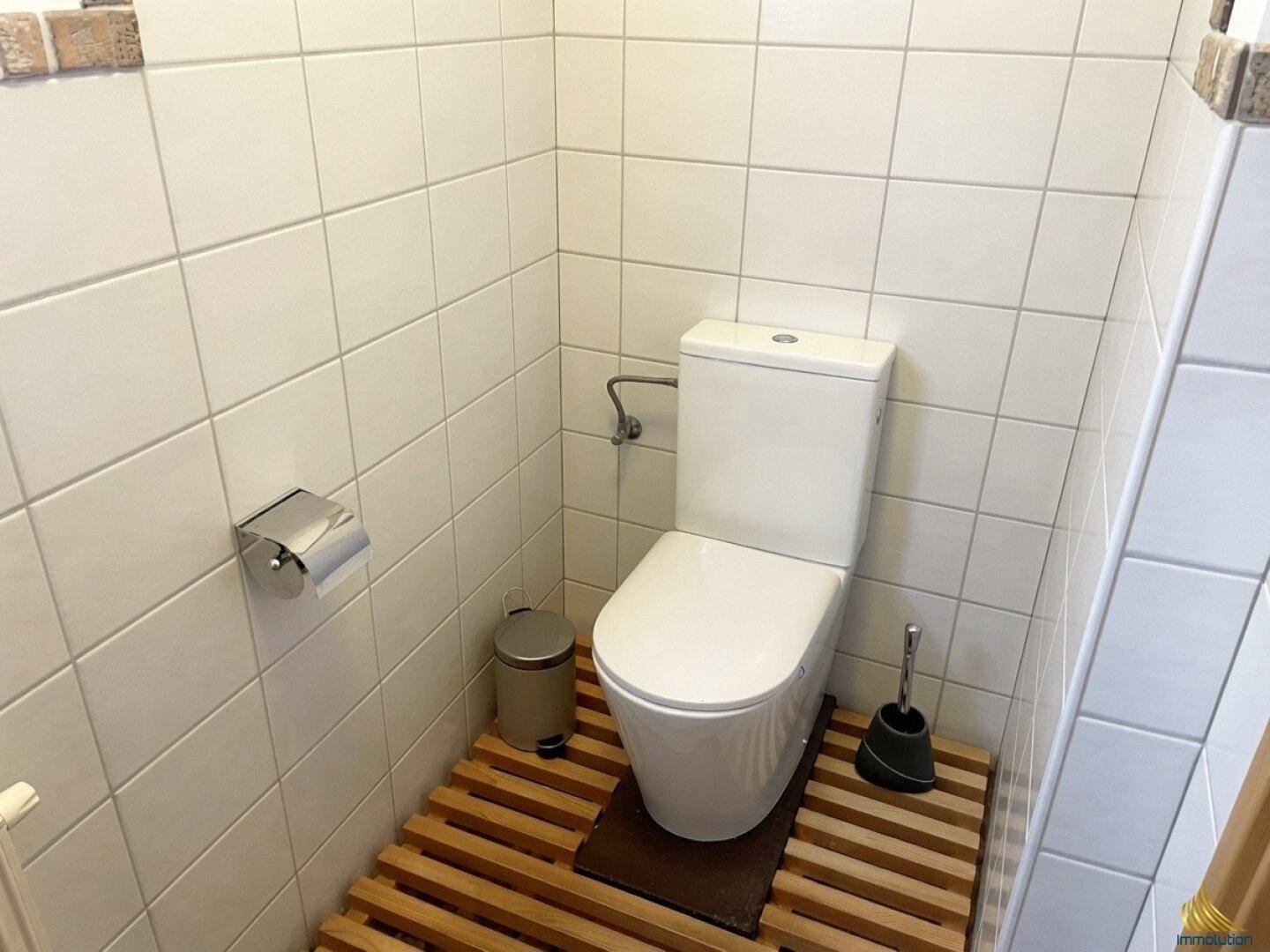 Kleines separates WC mit weißen Fliesen und Holzbodenrost für eine natürliche Optik.