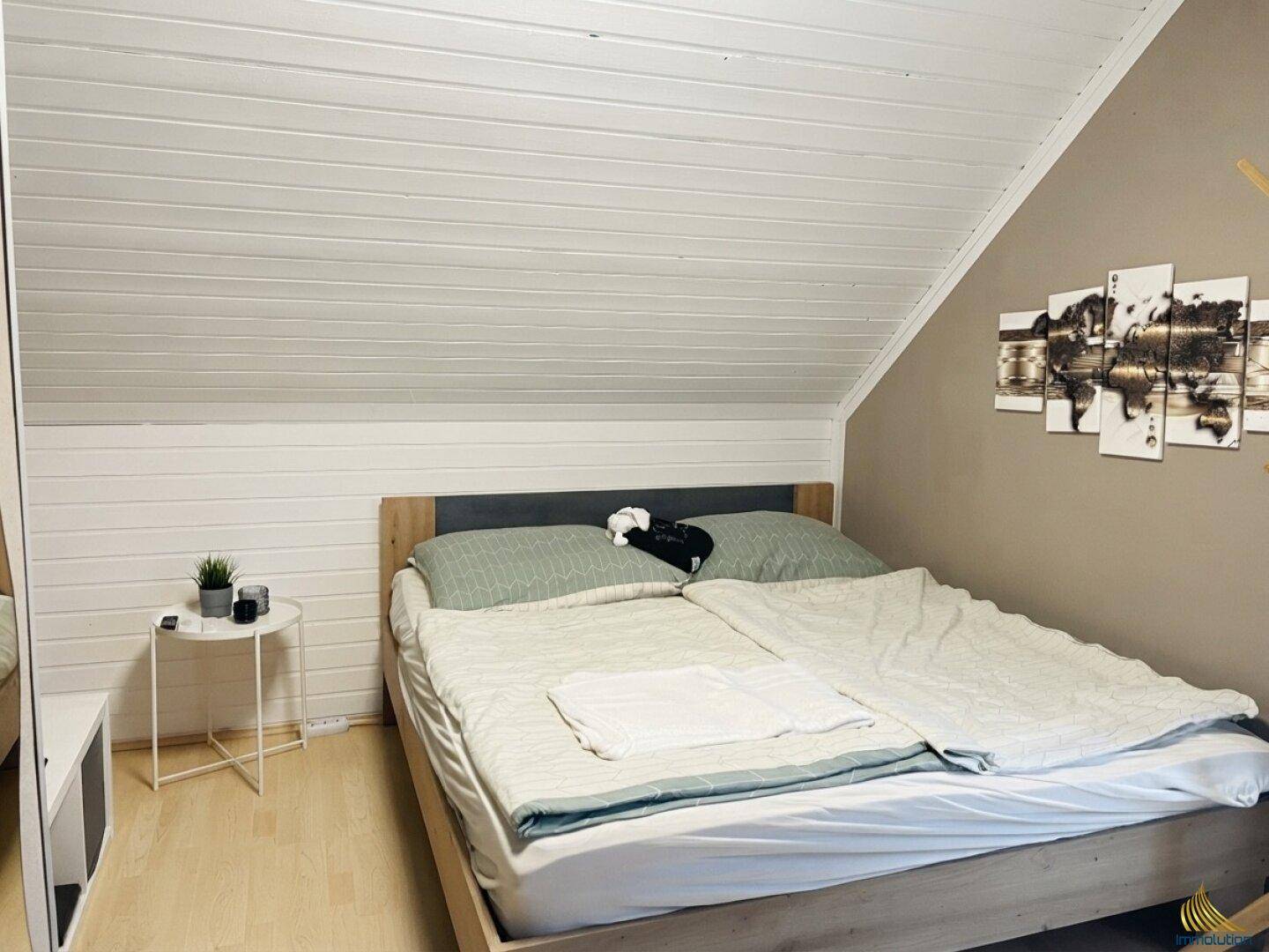 Gemütliches Schlafzimmer im Dachgeschoss mit Holzbett, Dachschräge und weißer Holzverkleidung.