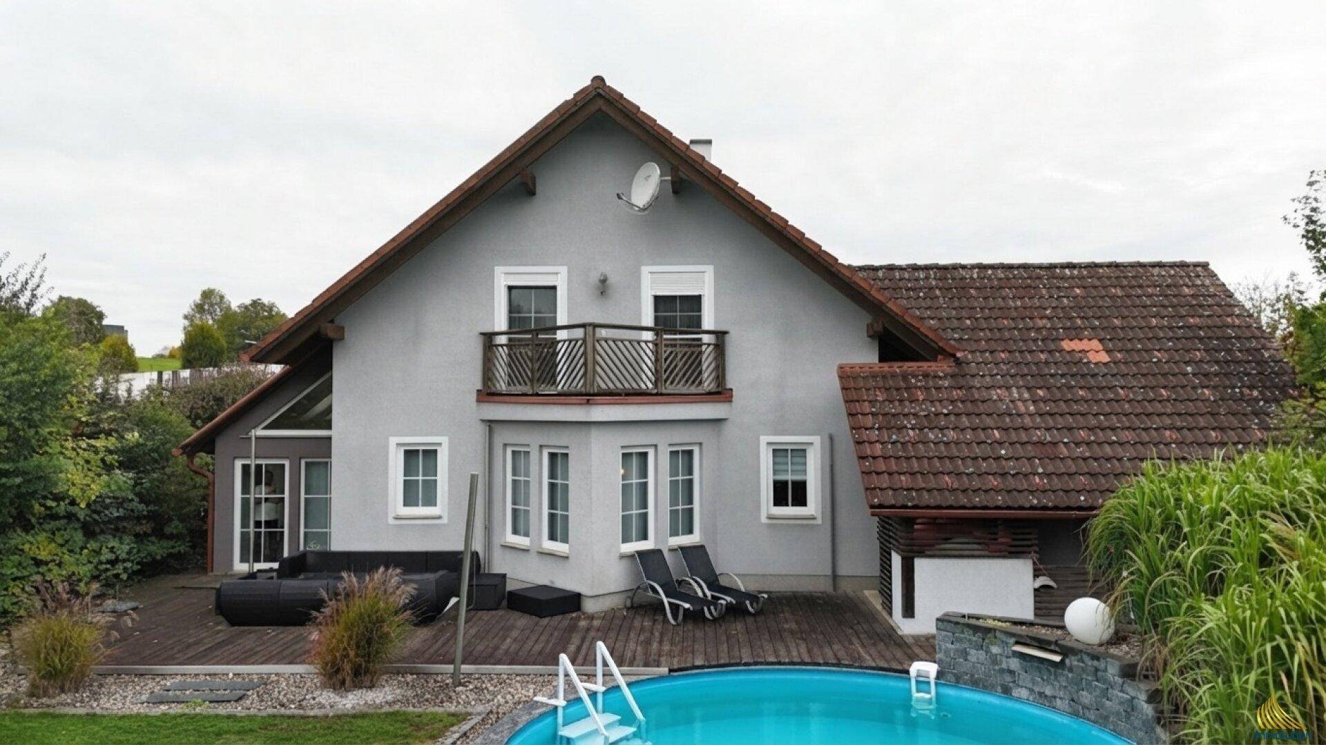 Einfamilienhaus mit Pool, Holzterrasse und Balkon im Grünen.