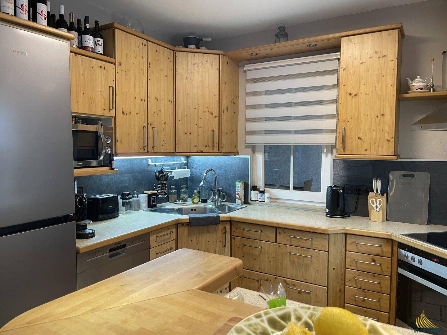 Gemütliche Holzküche mit Einbaugeräten, Fenster und viel Stauraum in den Oberschränken.