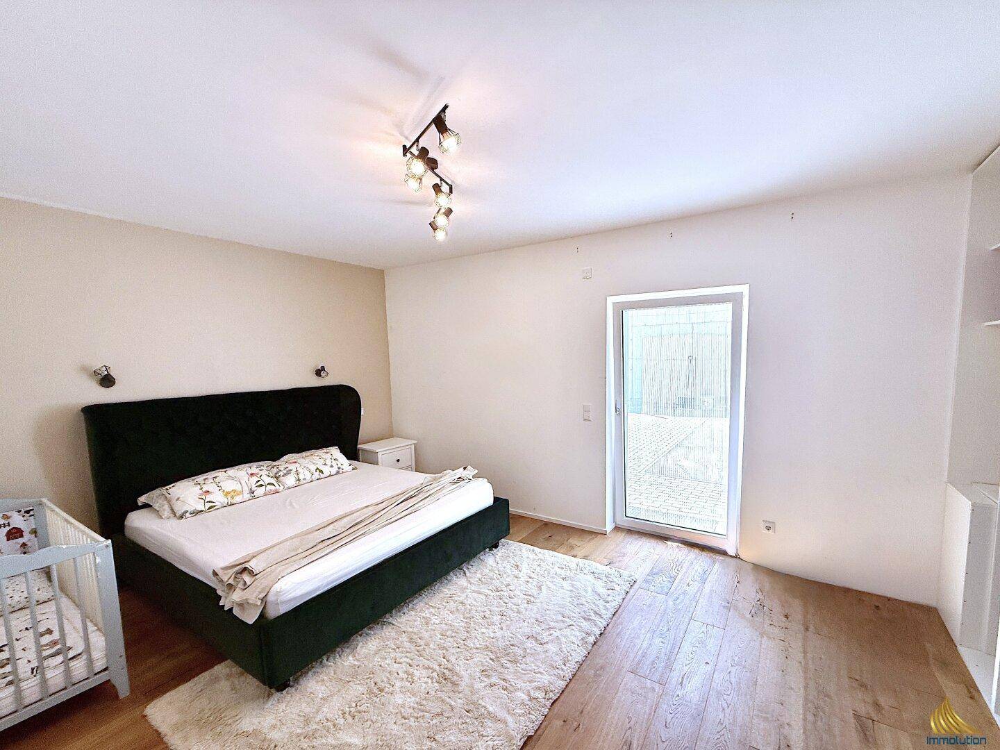 Geräumiges Schlafzimmer mit Holzboden, großem Bett und direktem Zugang zu einem Balkon.