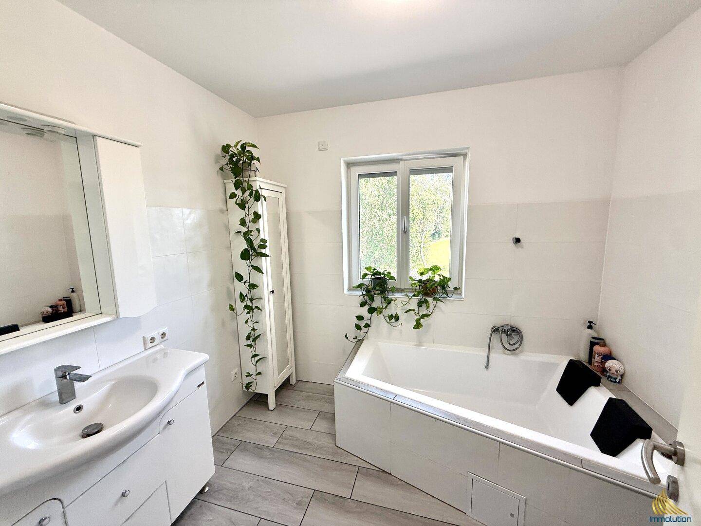 Modernes Badezimmer mit Badewanne, Waschbecken und Fenster für natürliche Belüftung.