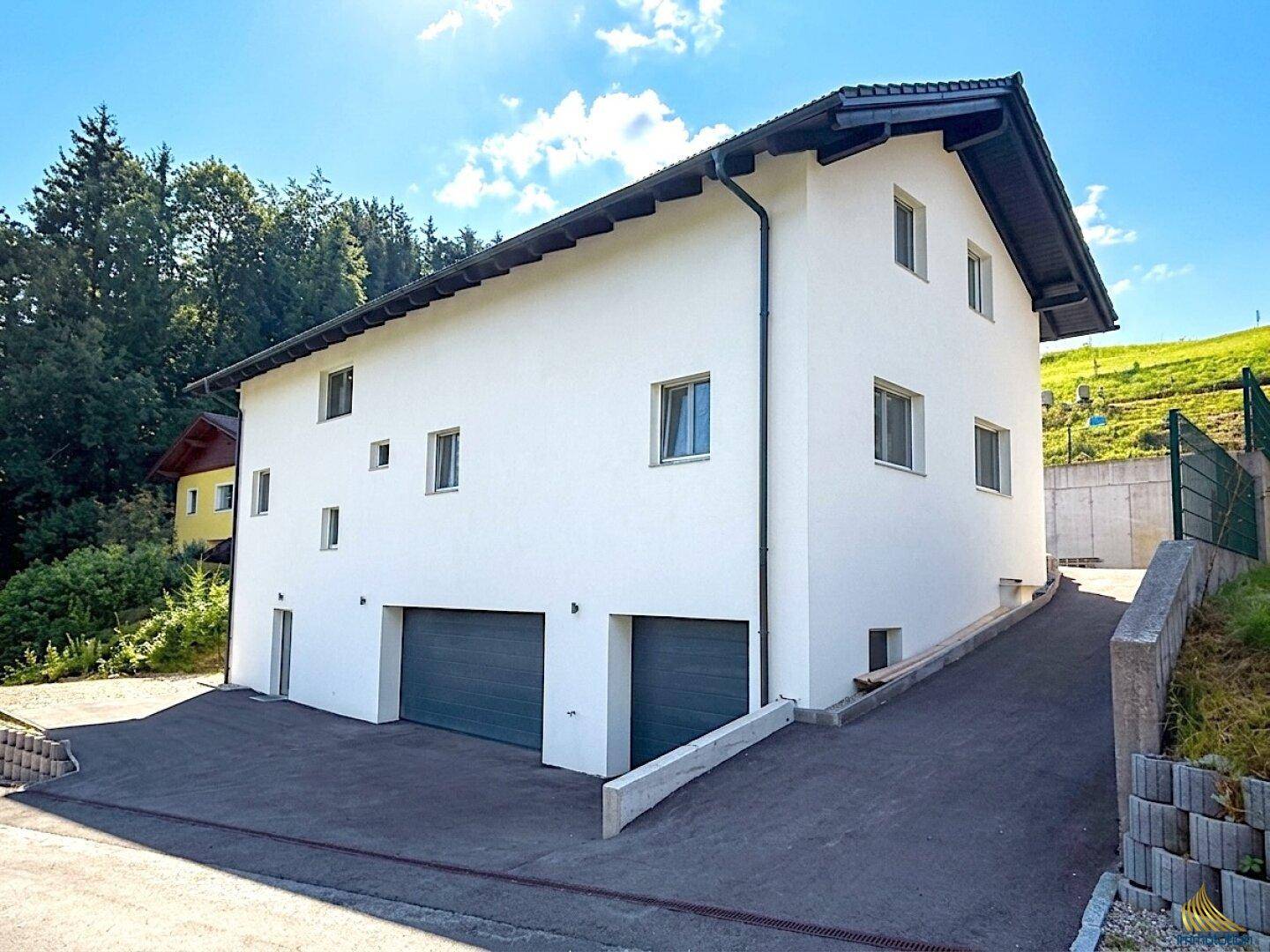 Modernes Einfamilienhaus mit weißer Fassade, zwei Garagen und einer gepflasterten Auffahrt.