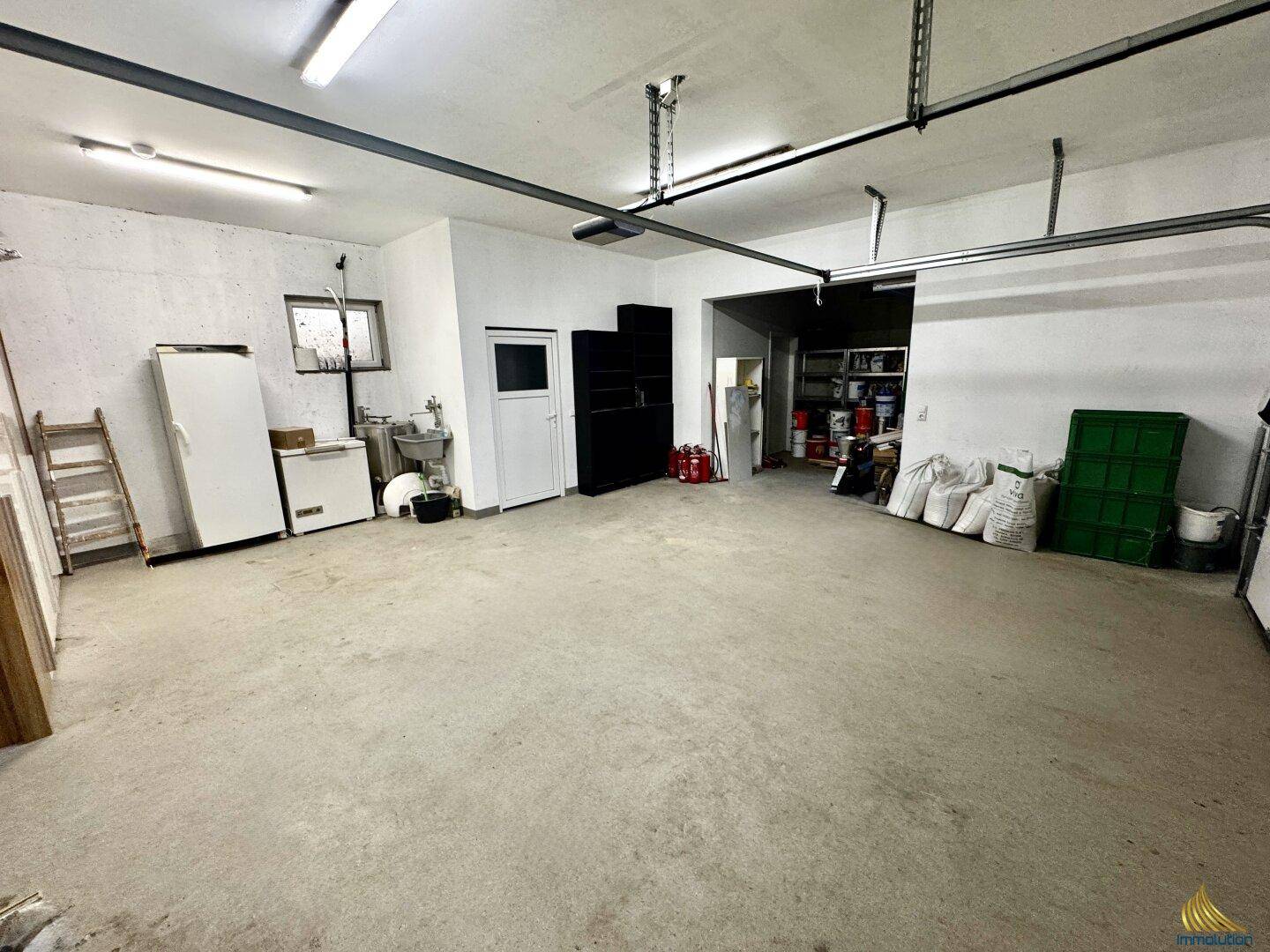 Geräumige Garage mit Betonboden, Stauraum und verschiedenen Geräten.