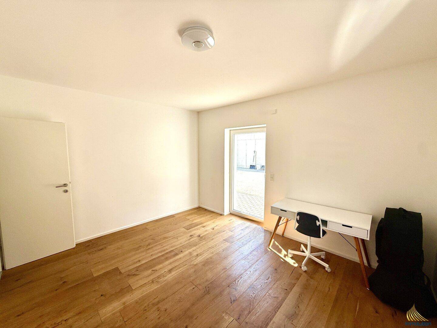 Helles Zimmer mit Holzboden, Schreibtisch und Zugang zu einem Außenbereich.