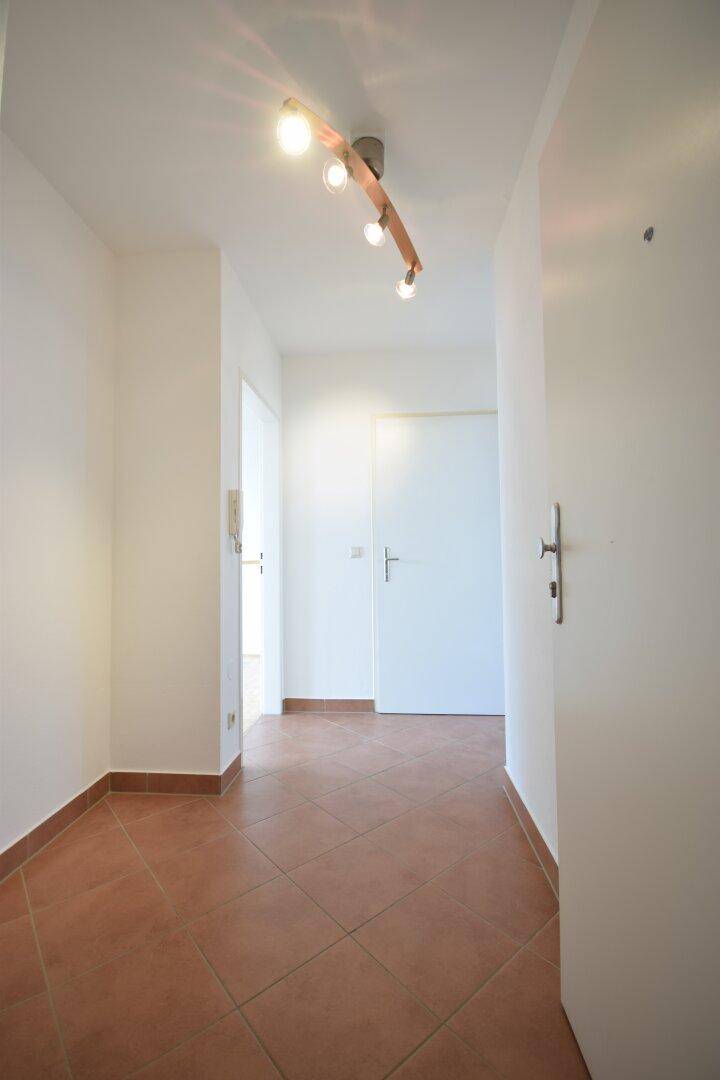 Heller Flur mit Terrakotta-Fliesenboden und moderner Deckenbeleuchtung, der zu weiteren Räumen führt.