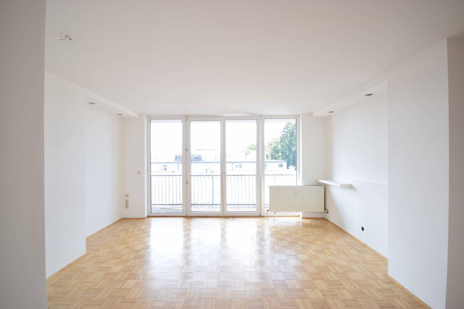 Geräumiges Wohnzimmer mit hellem Parkettboden und viel Tageslicht durch die großen Fenster.