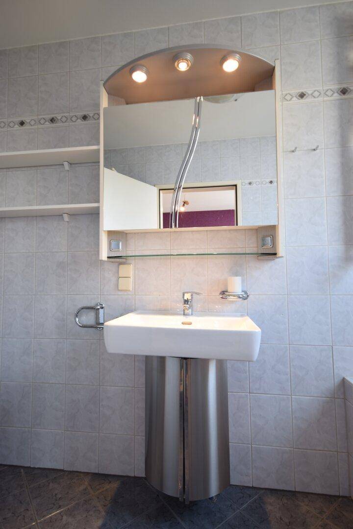 Modernes Badezimmer mit grau gefliesten Wänden, einem stilvollen Waschbecken und Spiegelschrank.