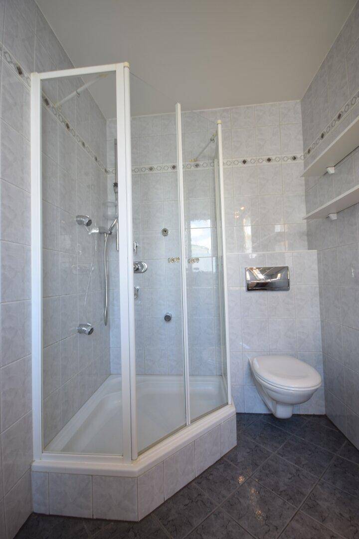 Badezimmer mit Eckduschkabine, wandhängendem WC und hellgrauen Fliesen an Wänden und Boden.