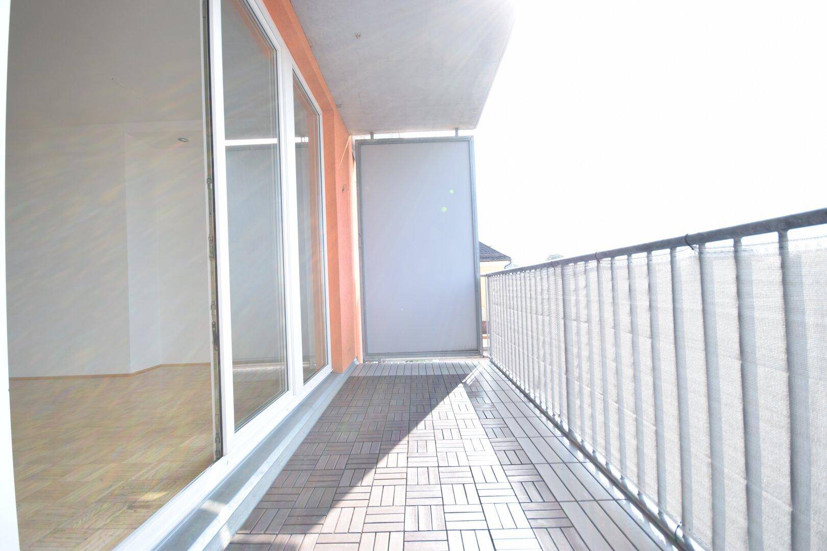 Heller Balkon mit Holzbodenfliesen und einem Geländer, der zum Entspannen im Freien einlädt.