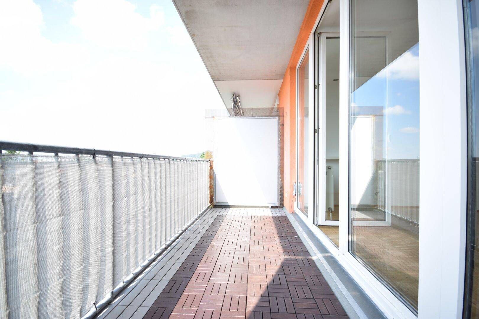 Geräumiger Balkon mit Holzbodenfliesen und einem Sichtschutz, ideal für sonnige Stunden.