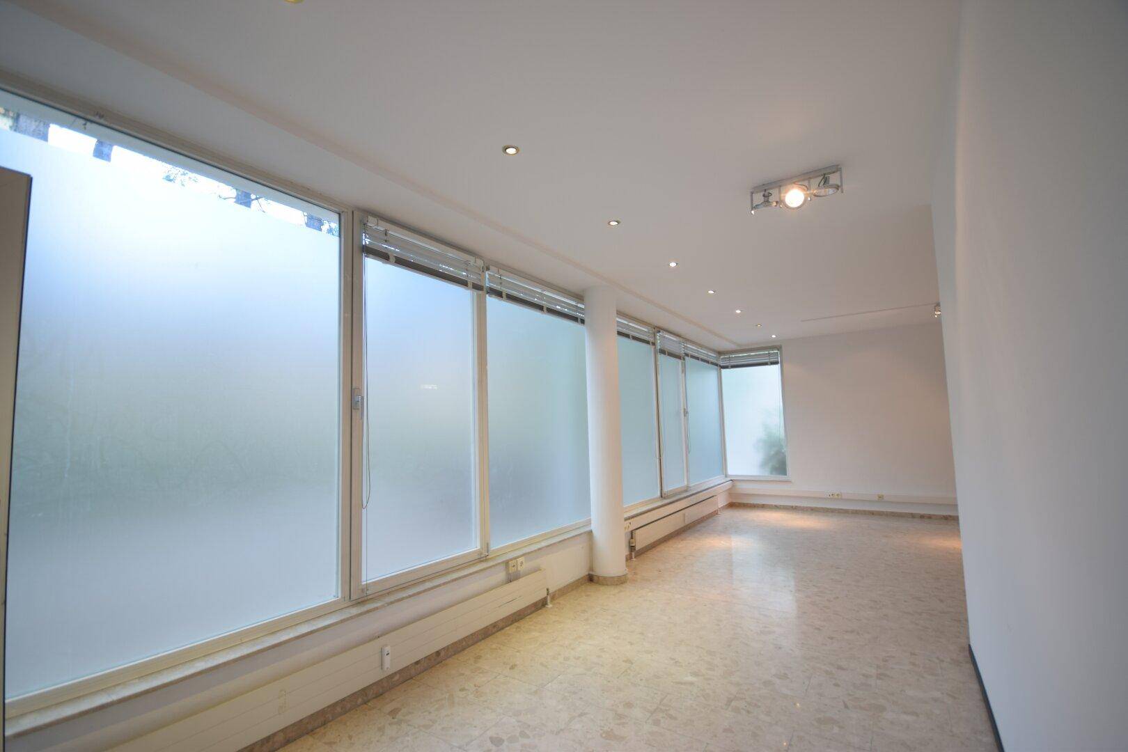 Geräumiger, heller Raum mit einer langen Fensterfront und hellem Fliesenboden, ideal für gewerbliche Nutzung.